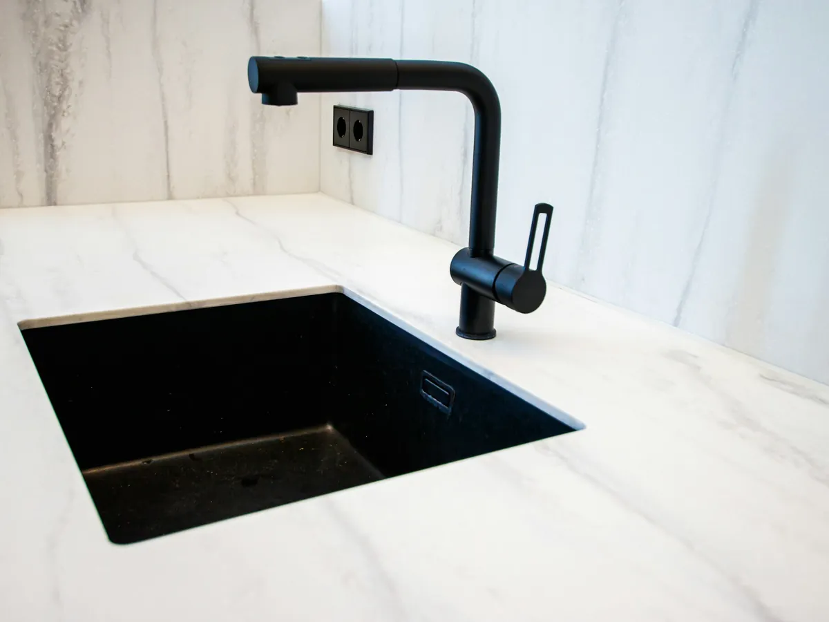 Matte black kitchen faucet over an undermount sink in a marble counter